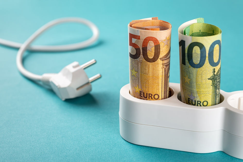 Euro money paper banknotes plugged into a white power strip over blue bacground. Increasing cost of electricity for business users and residential customers. Rise in electricity prices concept. 