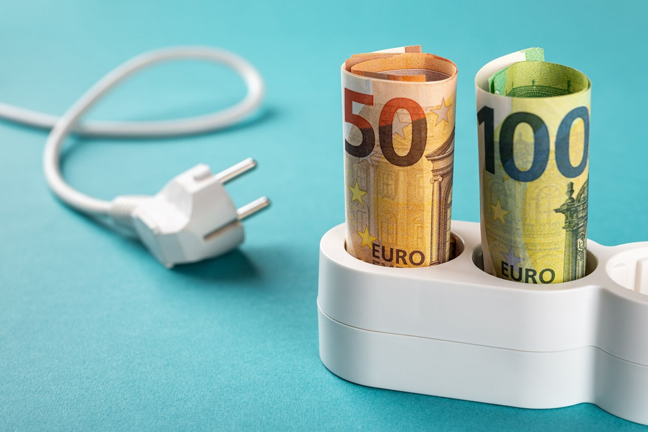 Euro money paper banknotes plugged into a white power strip over blue bacground. Increasing cost of electricity for business users and residential customers. Rise in electricity prices concept. 