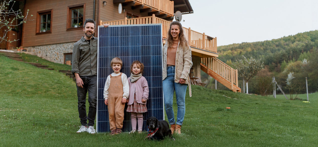 Junge Familie mit zwei Kindern steht auf einer WIese vor einem Solarpanel