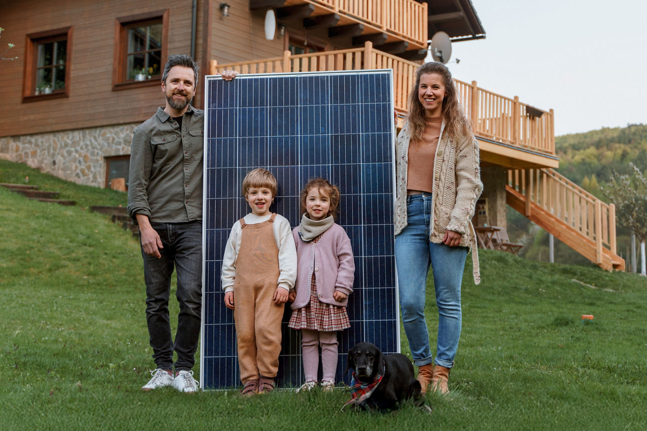 Junge Familie mit zwei Kindern steht auf einer WIese vor einem Solarpanel