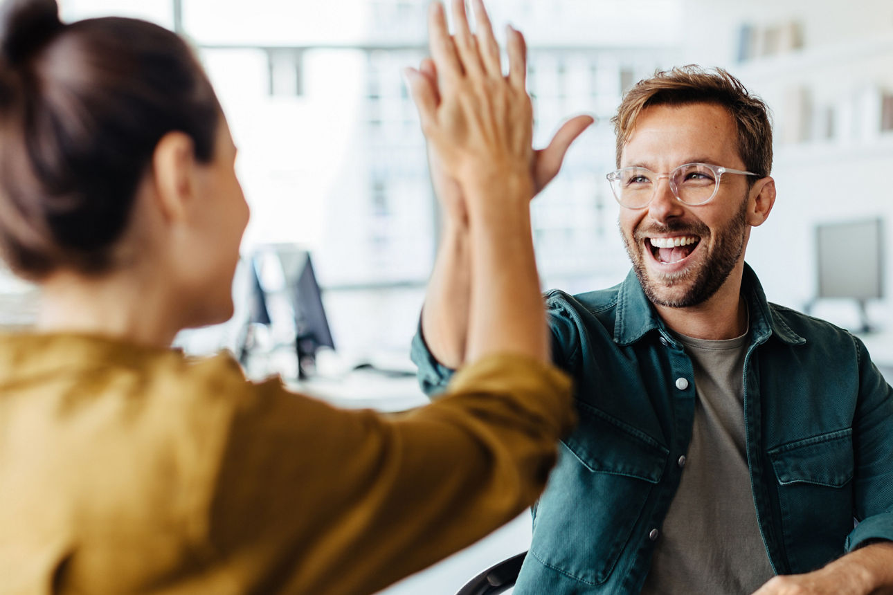 Drei Leute sitzen zusammen an einem TIsch, zwei davon klatschen lachend ab