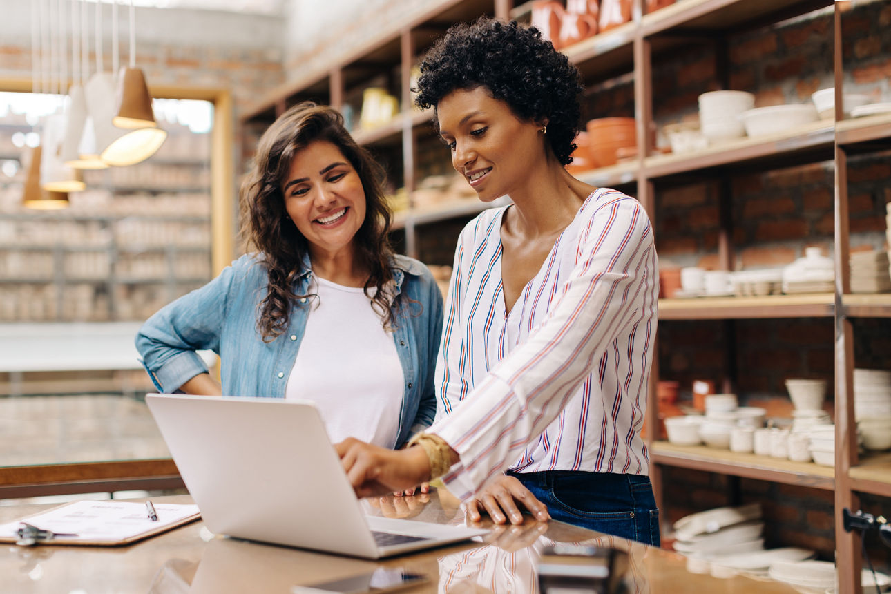 Zwei junge Geschäftsfrauen stehen vor einem Regal und schauen sich das Geschäftskonto im OnlineBanking an