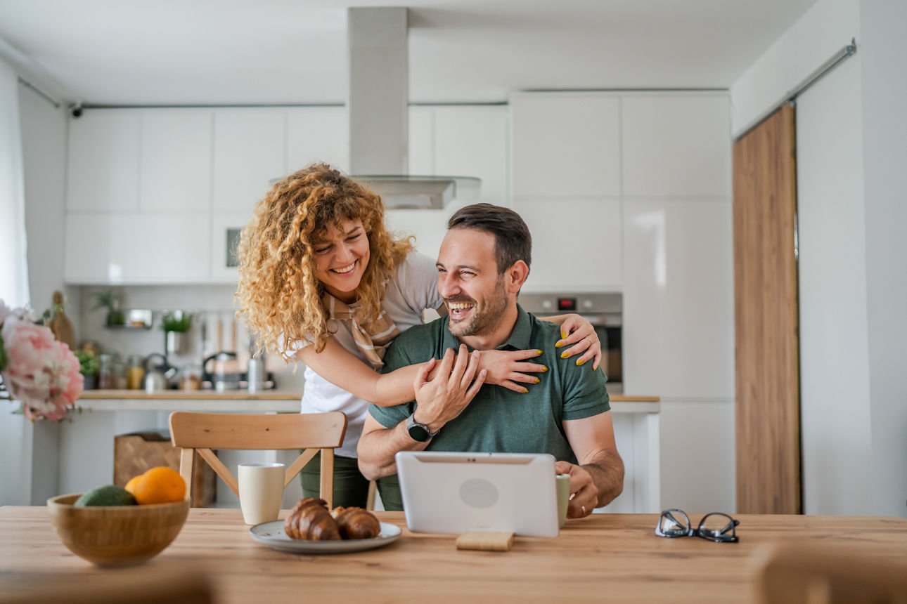 Ein Paar sitzt gemeinsam an einem Esstisch und guckt gemeinsam auf einen Laptop