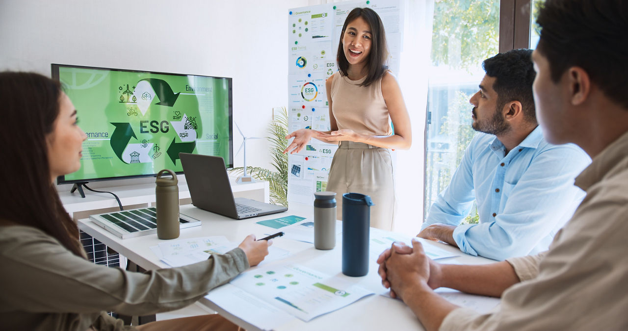Vier Personen in einem Besprechungsraum, eine Person präsentiert etwas an einem Bildschirm zum Thema ESG