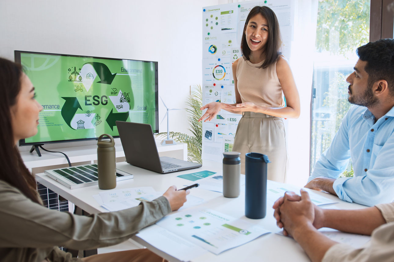 Vier Personen in einem Besprechungsraum, eine Person präsentiert etwas an einem Bildschirm zum Thema ESG