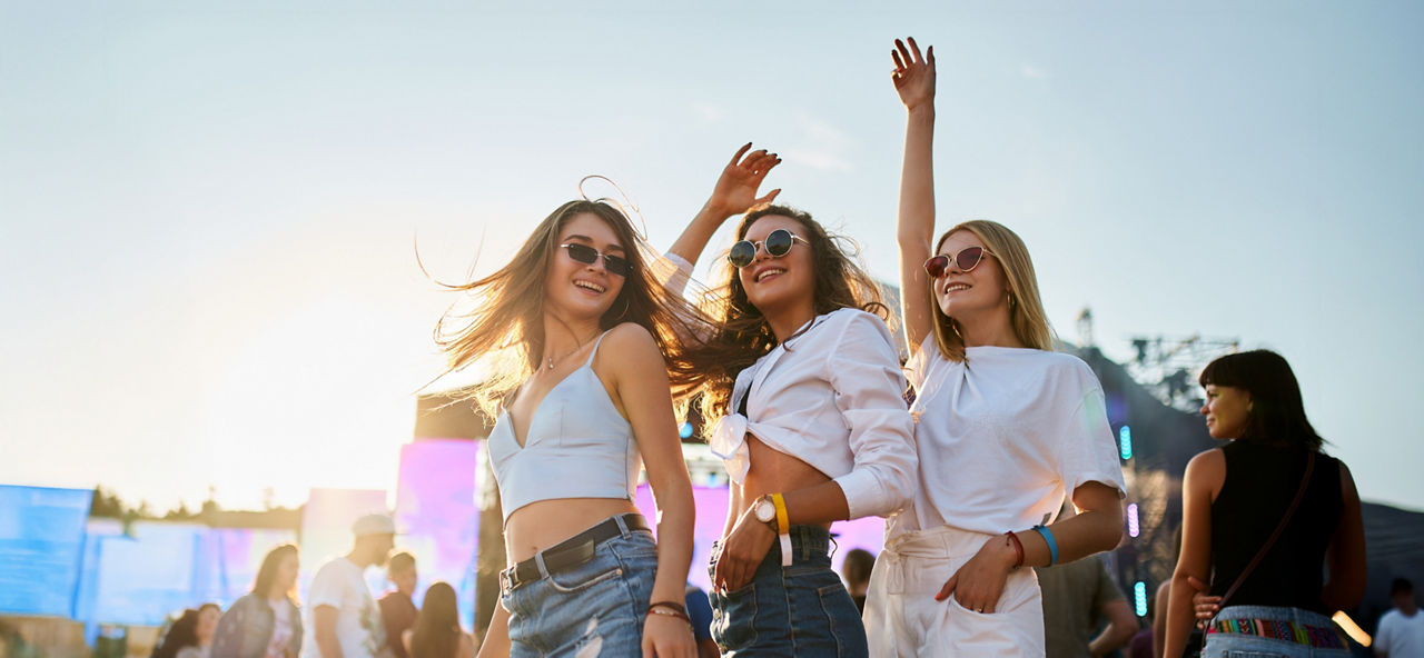 Drei junge Frauen tanzen fröhlich vor einer Bühne