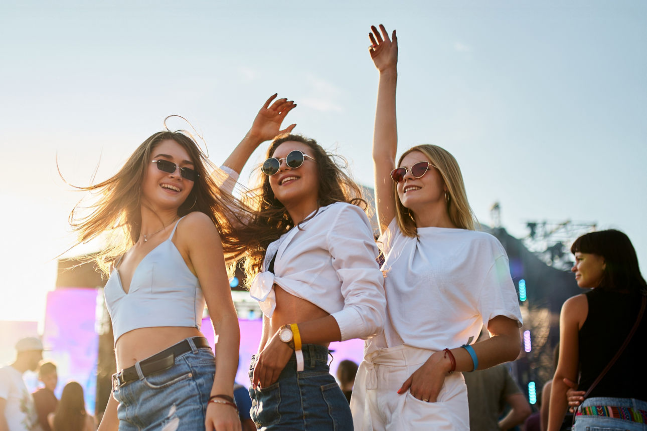 Drei junge Frauen tanzen fröhlich vor einer Bühne