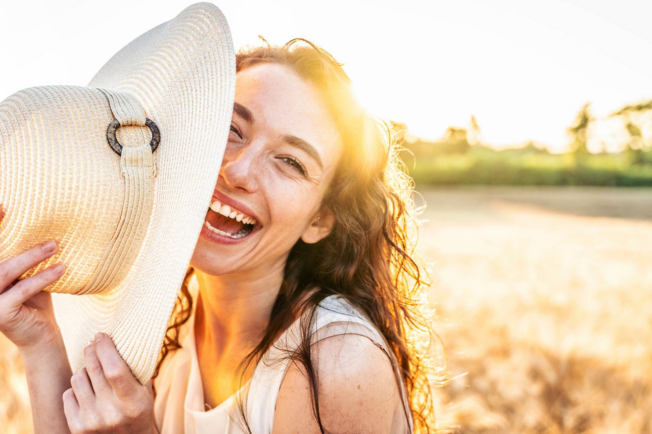 Frau mit Hut in der Hand lacht