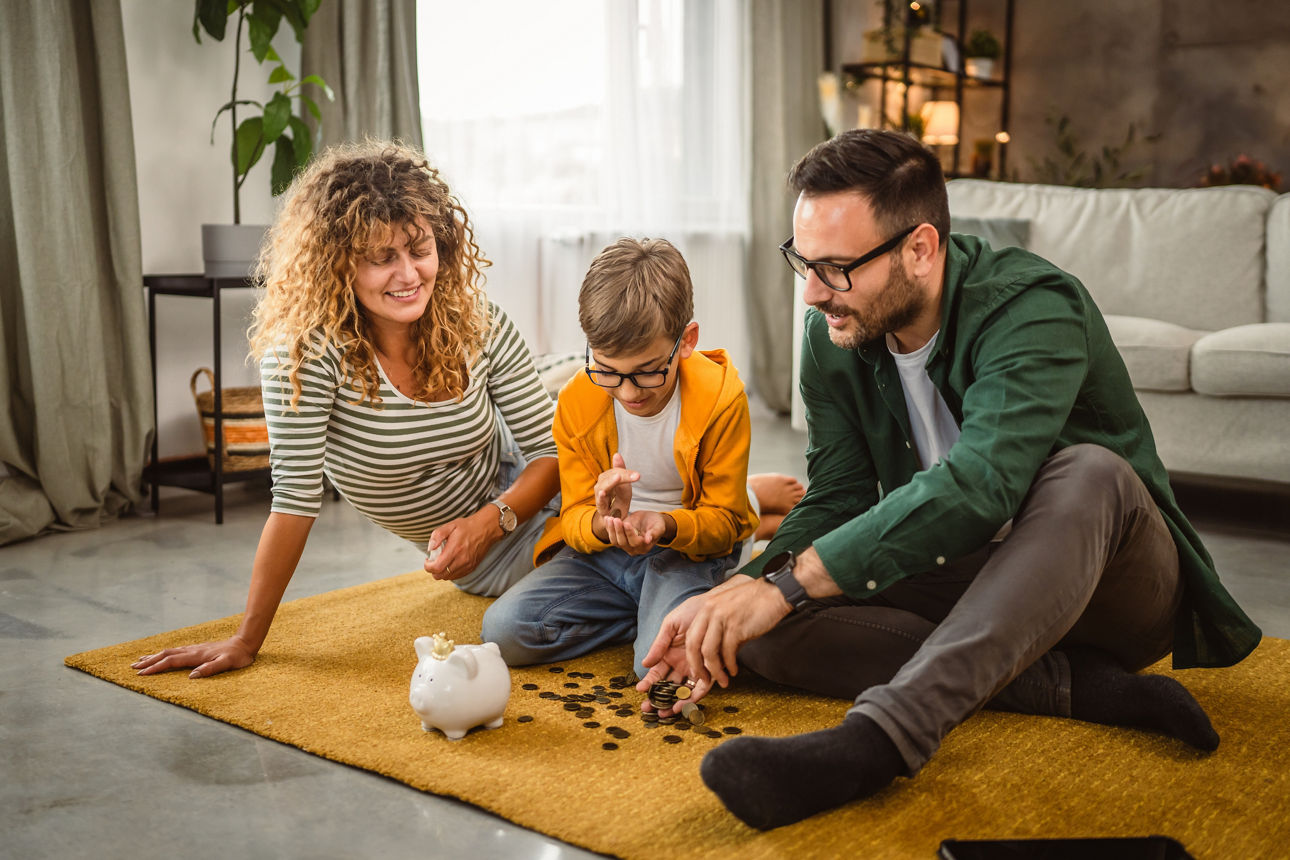Eine Familie sitzt zusammen im auf einem Teppich und zählt Münzen aus einem Sparschwein