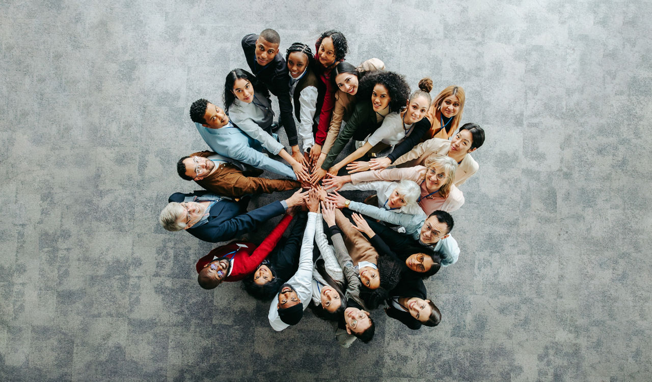 Eine Gruppe von vielen unterschiedlichen Menschen, die die Hand aufeinanderlegen