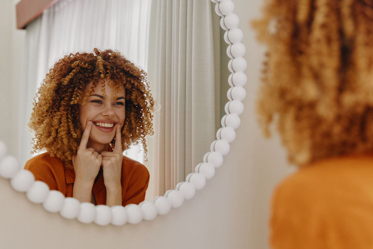 Eine Frau steht lachen vor einem Spiegel