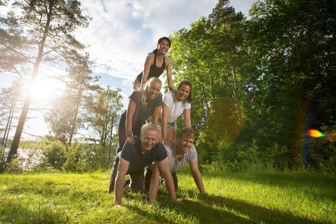 5 Menschen machen eine Menschenpyramide und klettern aufeinander auf einer Wiese