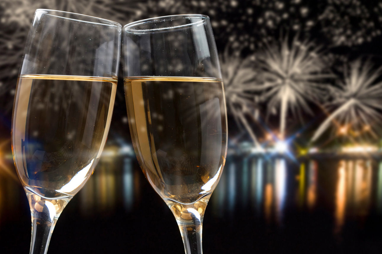 Zwei Sektgläser mit Feuerwerk im Hintergrund.