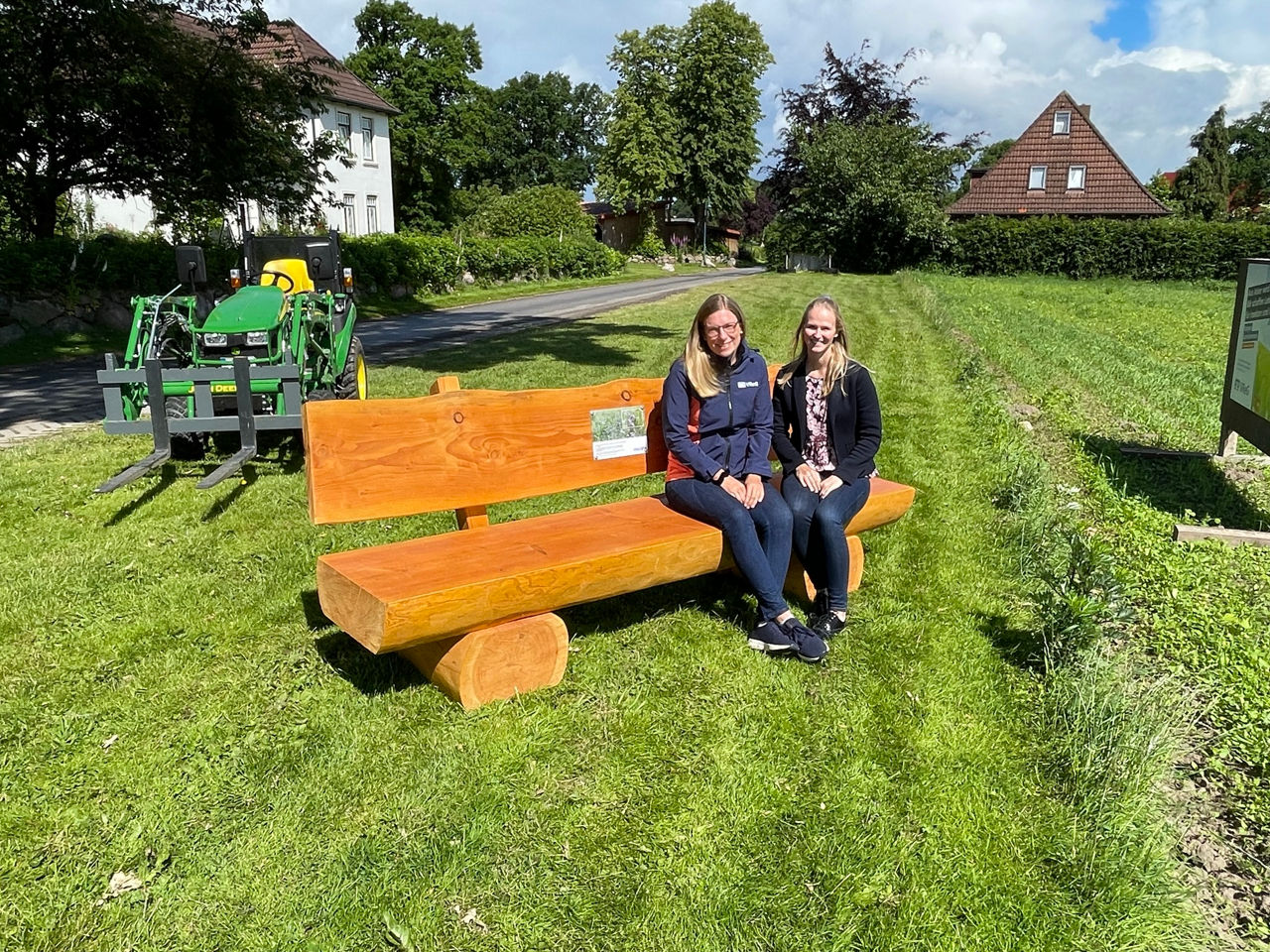 Zwei Frauen sitzend auf einer Holzbank im Freien.