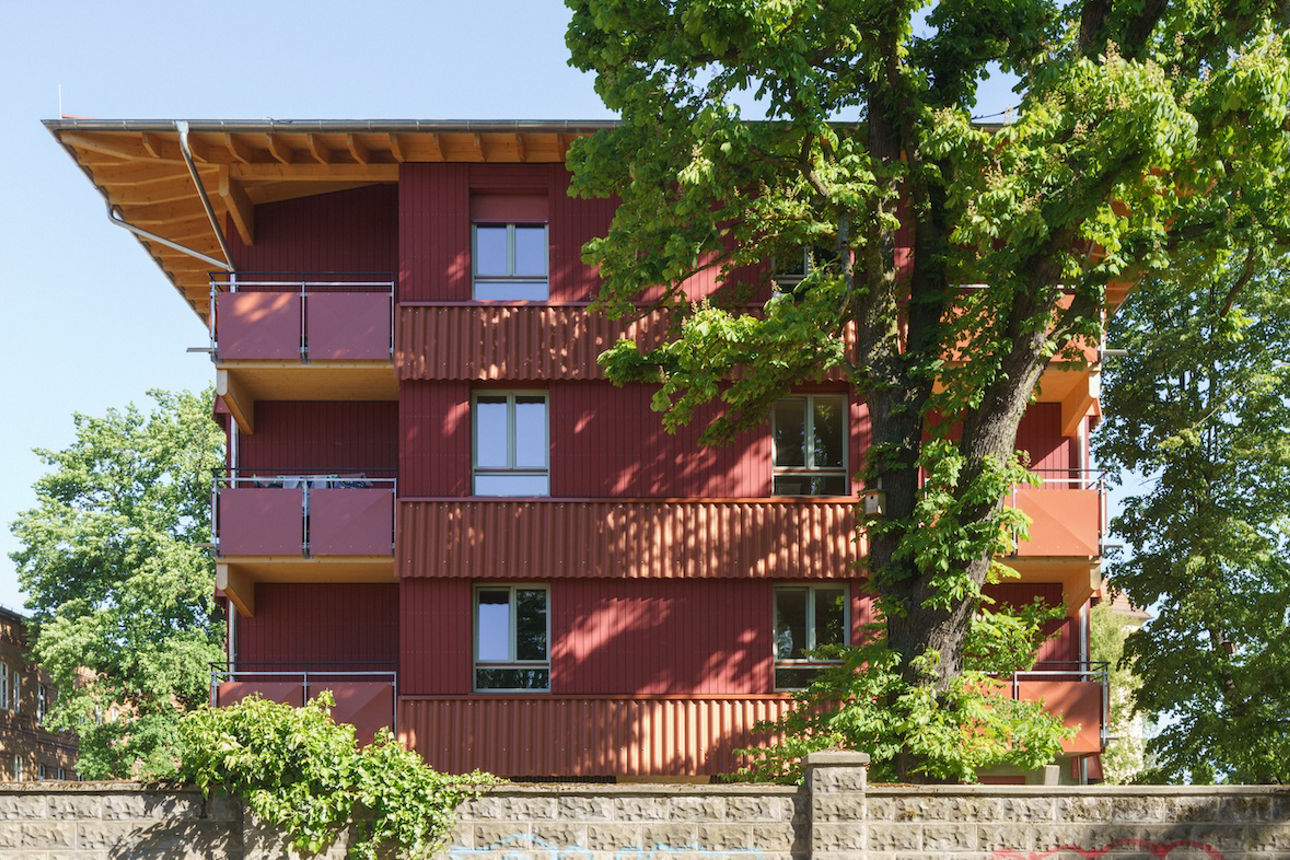 Seitenansicht des roten Haus im Park. Es ist teilweise von einer Mauer verdeckt.