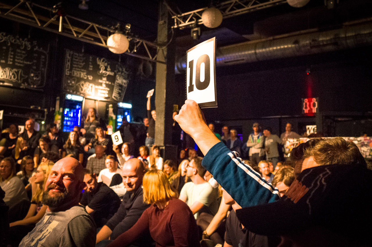 Viele Menschen sitzen in einer Halle und eine Person hält ein Schild mit einer 10 hoch.