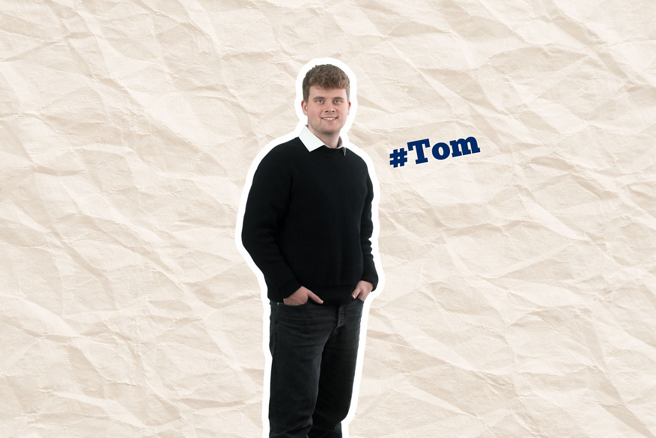 Junger Berufstätiger in einem schwarzen Poloshirt, hellen Jeans und einer Armbanduhr.