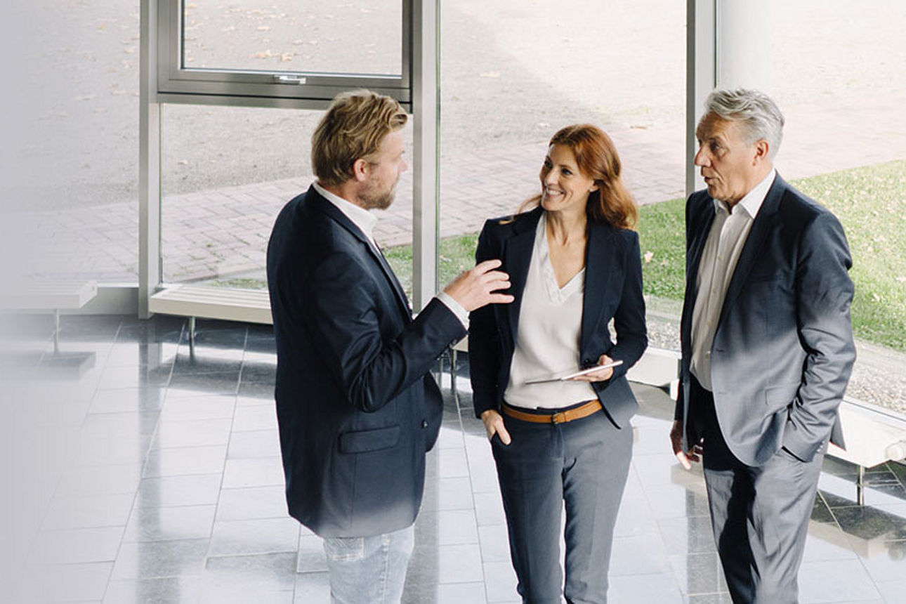 Diese Förderprogramme kommen für Sie infrage - Eine Frau und zwei Männer im Anzug im Gespräch