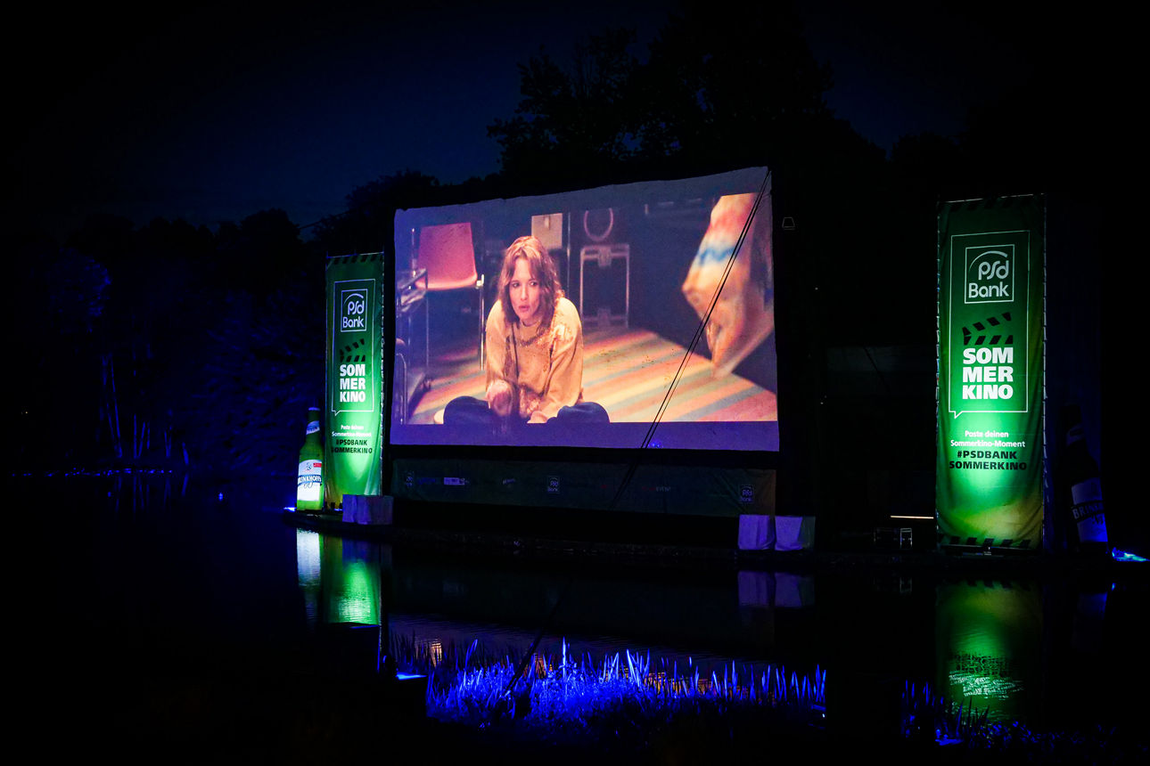 Fotografie der Leinwand beim PSD Bank Sommerkino auf dem ein Blockbuster zu sehen ist.
