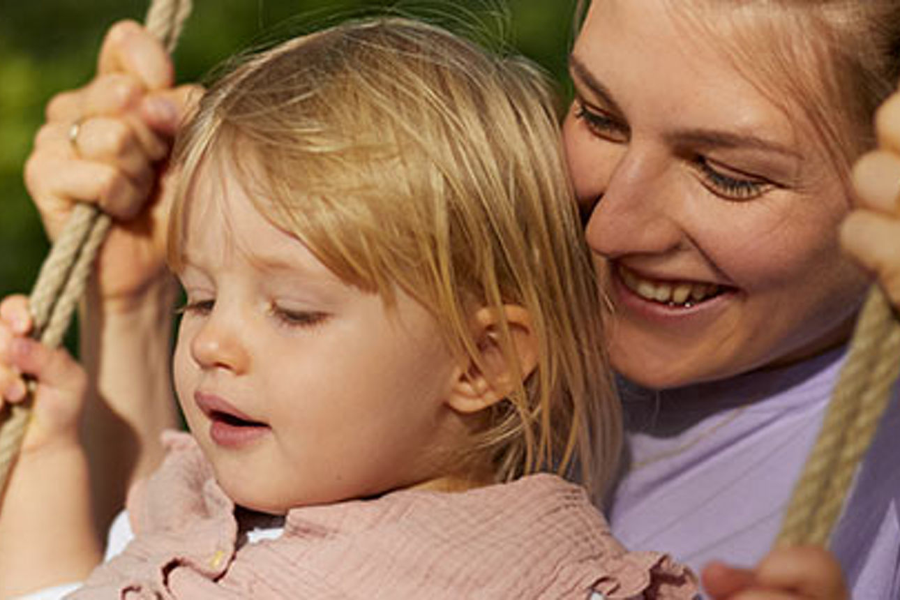 Frau Schaukelt mit Kind im Garten