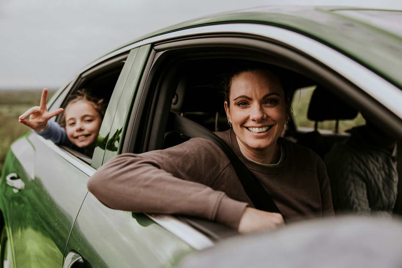 Eine Mutter und ein Kind sitzen in einem Auto und schauem zum geöffneten Fenster raus. 