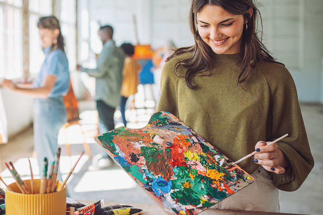 Eine junge Frau in einem Atelier tupft Farbe auf einen Pinsel