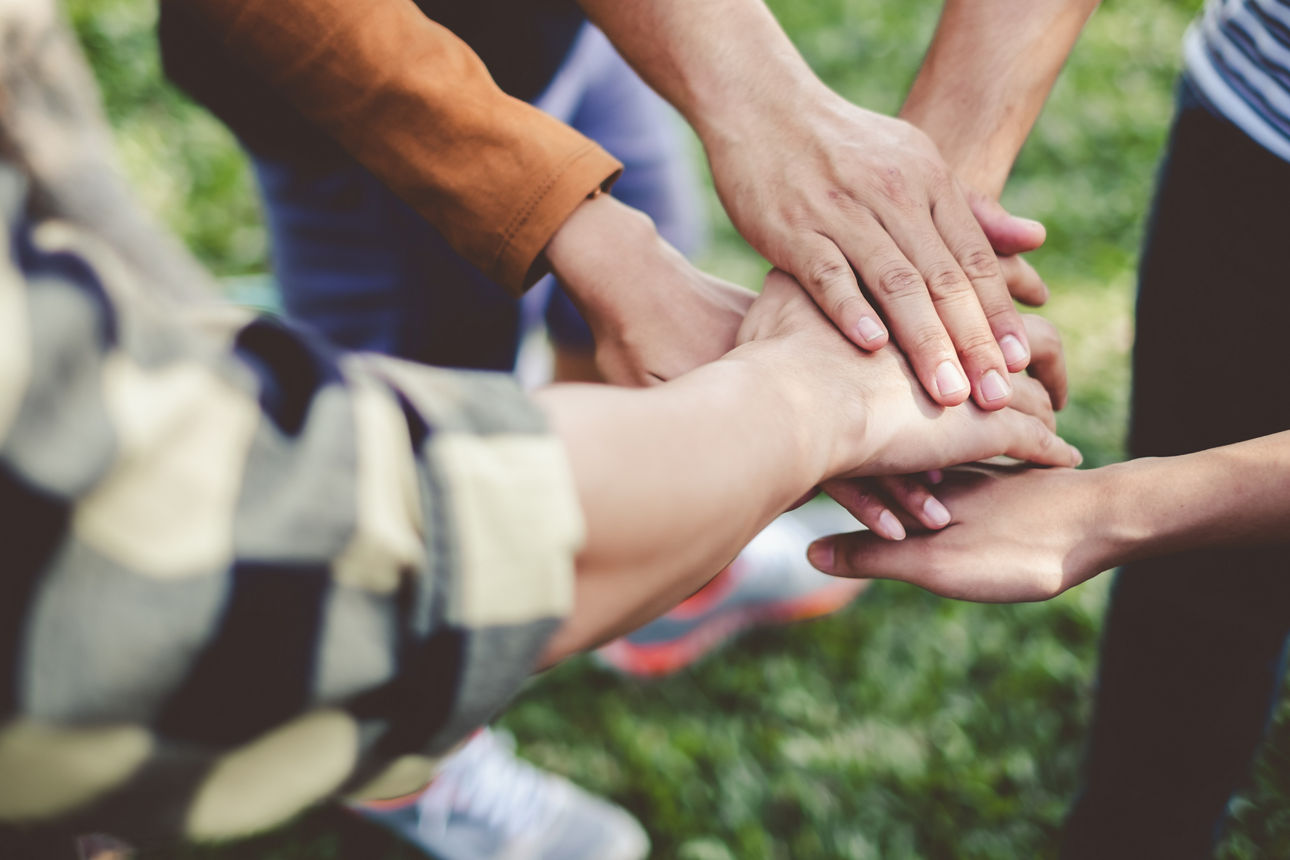 Mehrere Menschen legen ihre Hände übereinander uund symbolisieren so Gemeinschaft