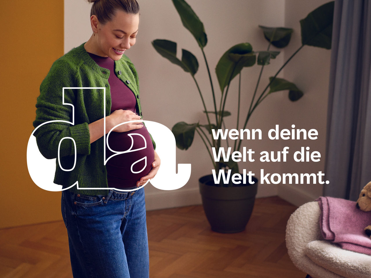 Eine Frau in freudiger Erwartung steht in einem Zimmer und hält sich lächelnd den Bauch.