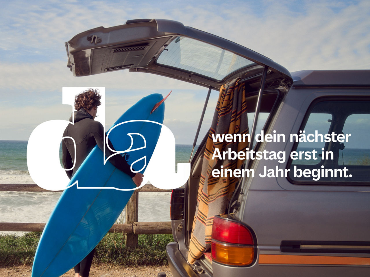 Ein Surfer mit einem Surfbrett blickt auf das Meer hinaus.