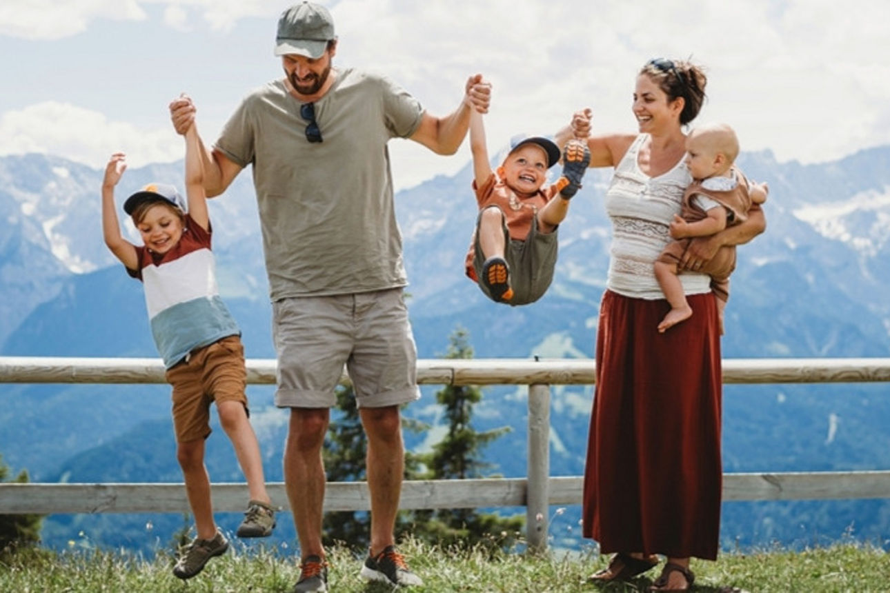 Eine Familie mit drei Kindern haben Spaß vor einer Bergkulisse