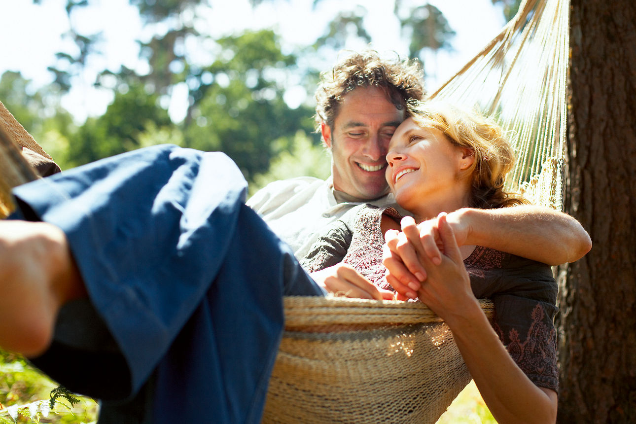 Ein Paar liegt lächelnd umschlungen in einer Hängematte.