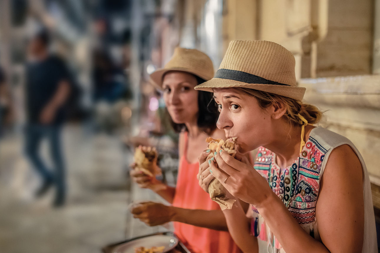 Zwei Frauen essen in entspannter Atmosphäre auf einer belebten Straße einen Snack.