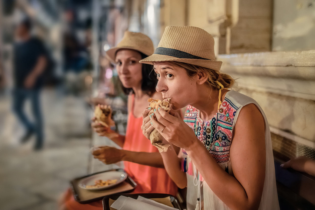 Zwei Frauen essen in entspannter Atmosphäre auf einer belebten Straße einen Snack.