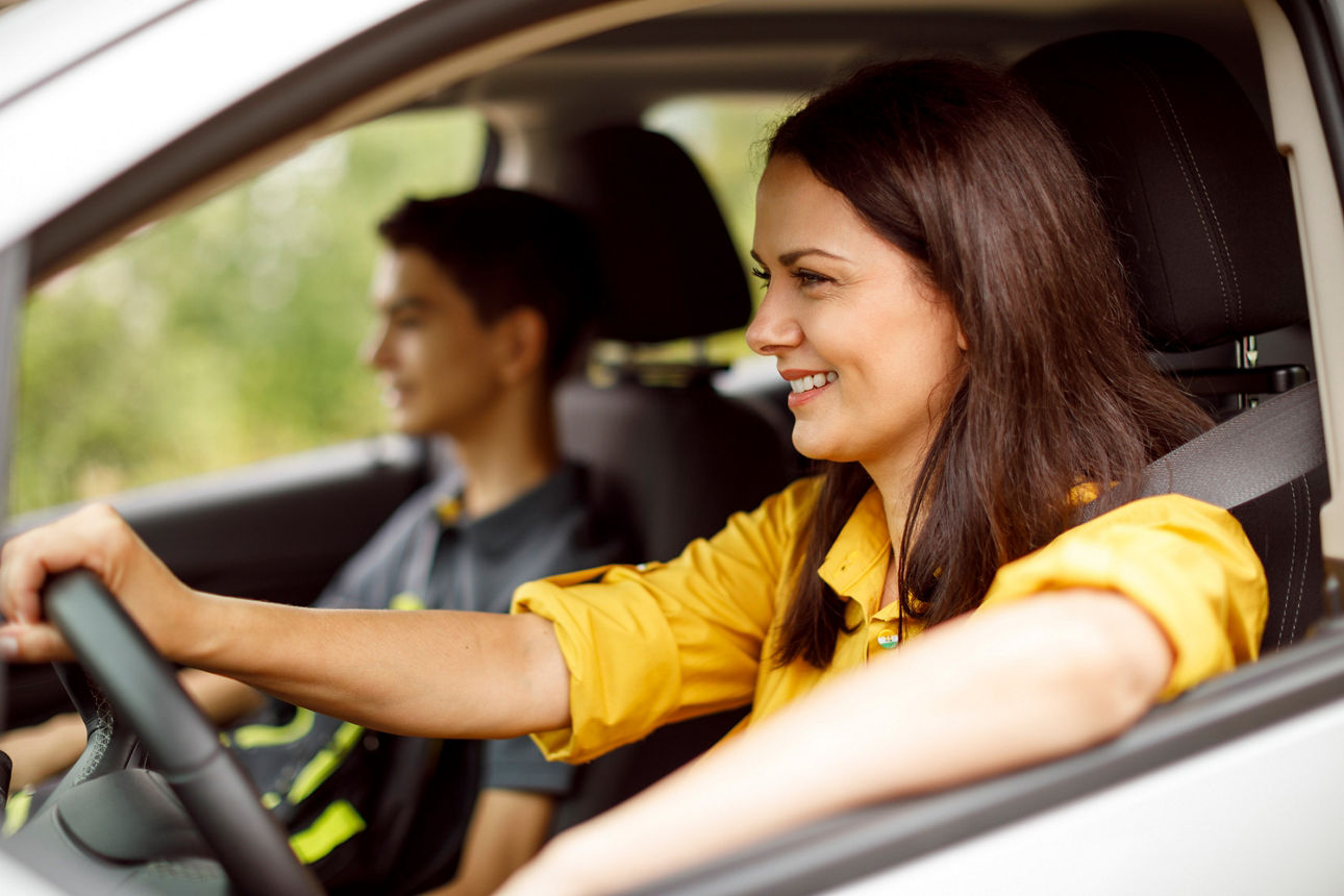 Eine junge Fahranfängerin fährt ihren Bruder im Auto als Symbol für das Sparen für den Führerschein der Kinder.