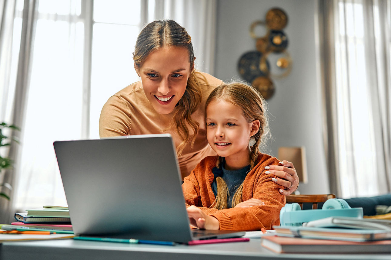  Lächelndes Patenkind mit seiner Patentante beim gemeinsamen Blick auf den Laptop, symbolisiert das Anlegen eines Sparbuchs z