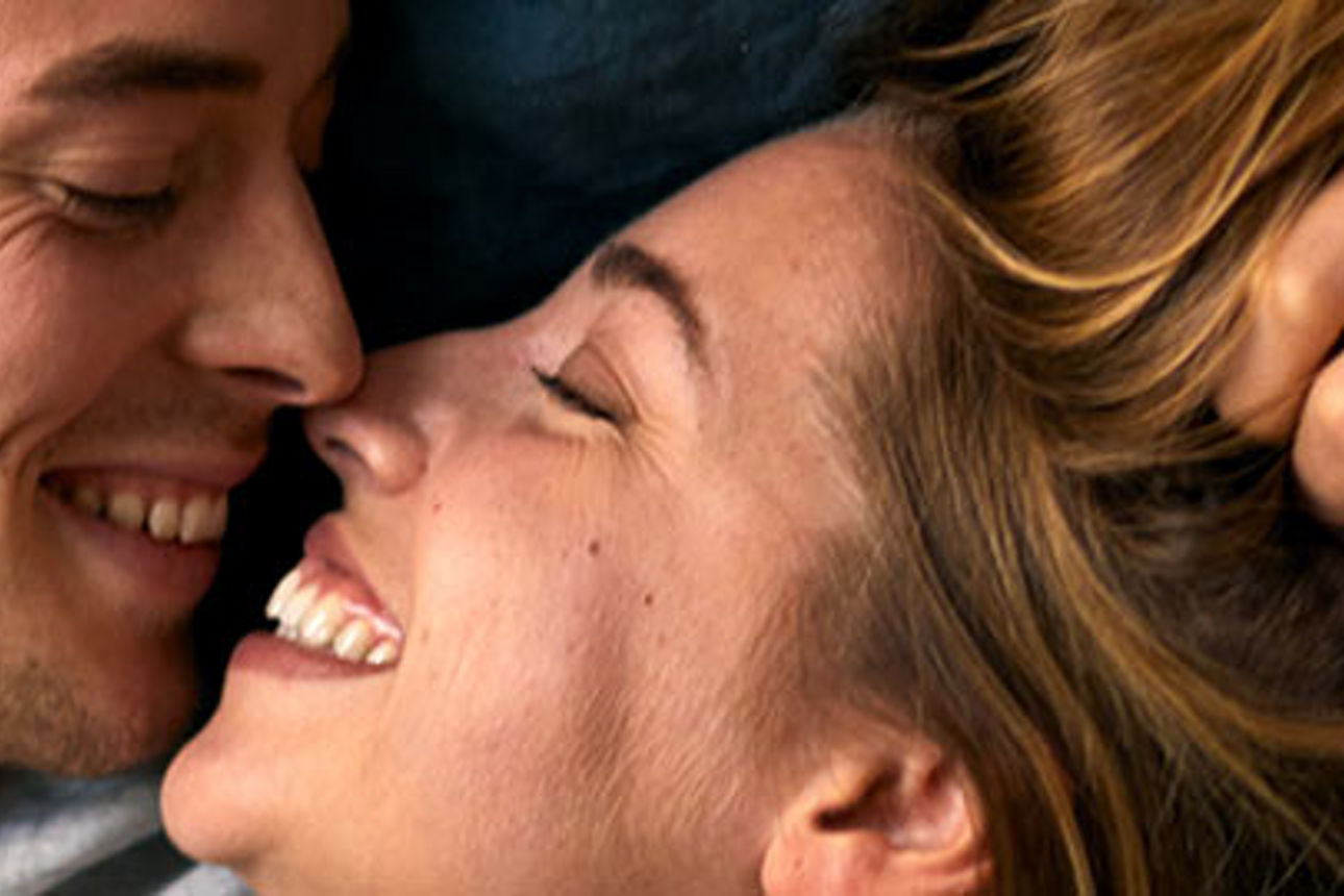 Ein Mann und eine Frau lächeln fröhlich, während sie zusammen im Bett liegen und eine warme und intime Atmosphäre schaffen.