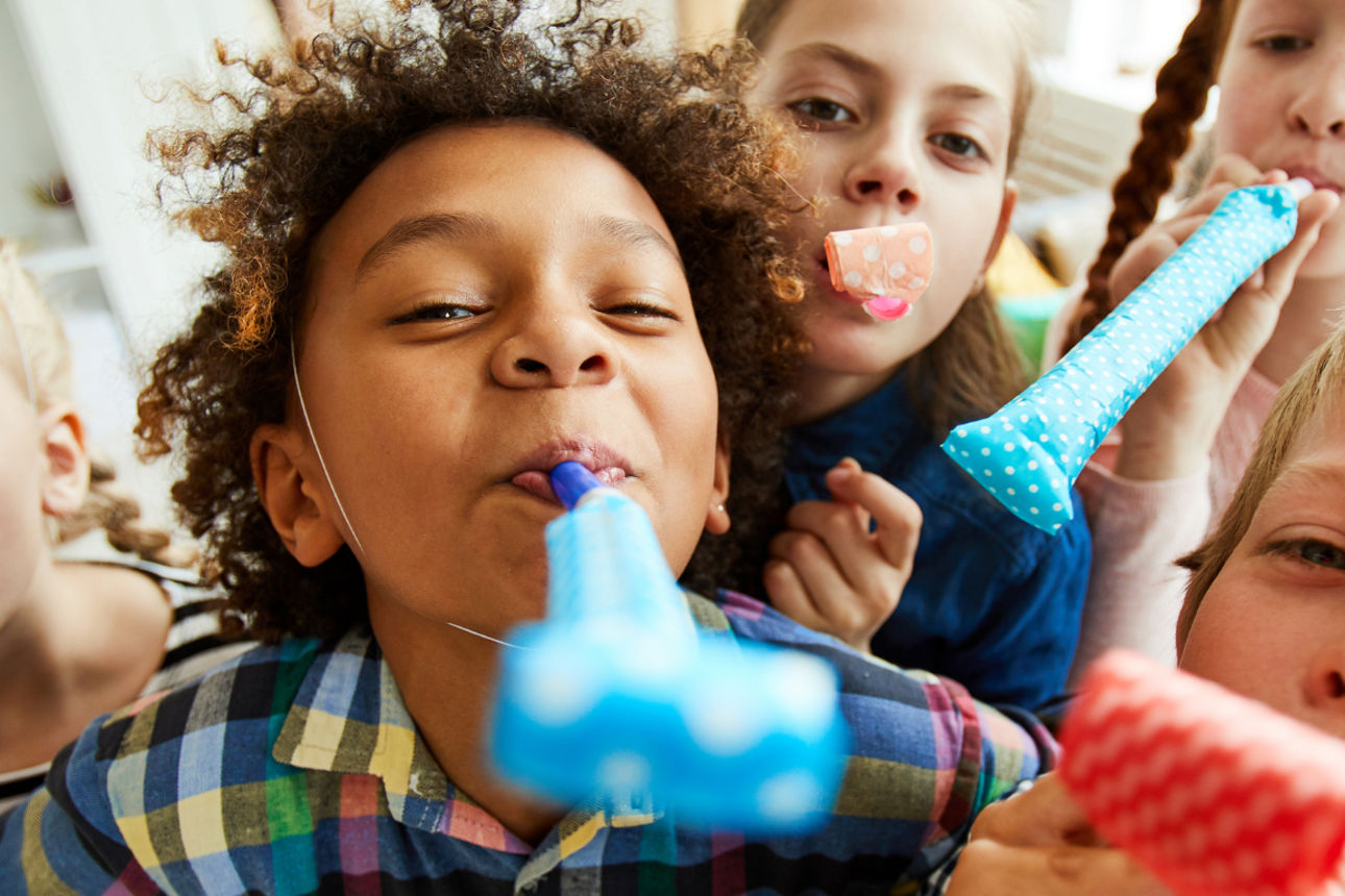 Kinder feiern gemeinsam mit Partytröten und festlicher Kleidung bei einer fröhlichen Veranstaltung.