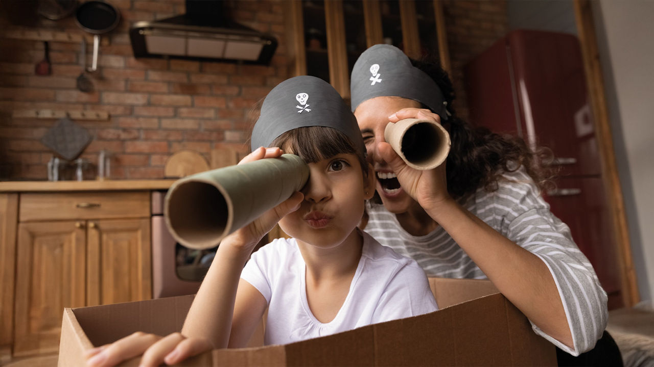 Mutter und Sohn spielen in der Küche in einem Karton Piraten. Sie halten Fernrohe aus Küchenrollen in den Händen.