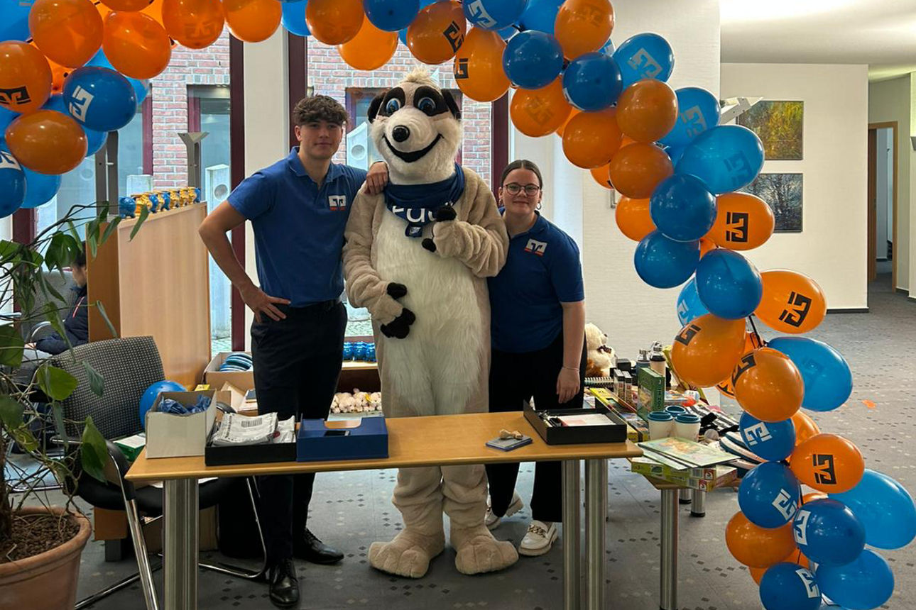 Maskottchen Eddie und zwei Mitarbeiter als Gruppenfoto am Kinderschalter