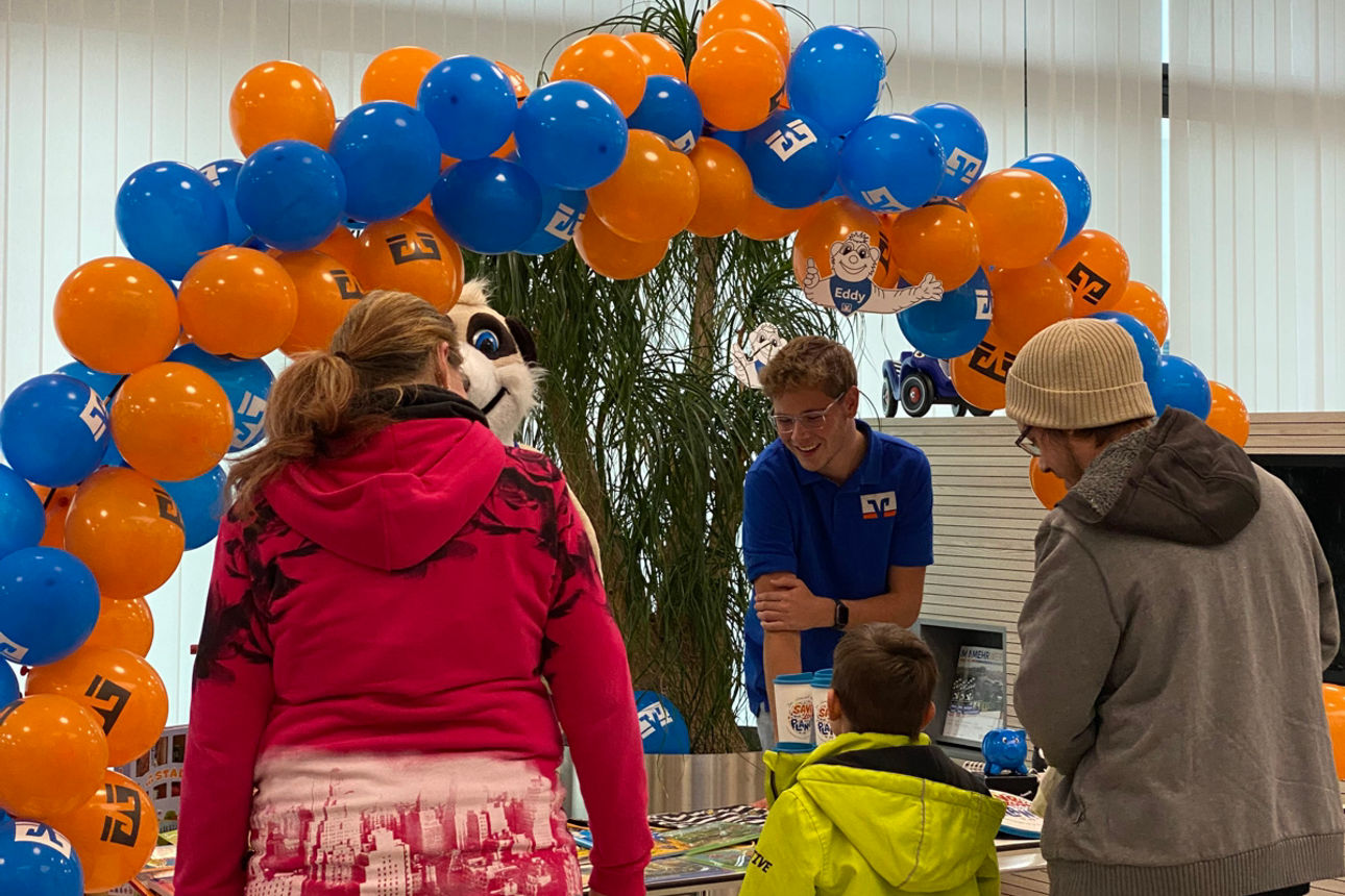 Familie vor dem Kinderschalter stehend. Kinderschalter mit Luftballon Schlange in blau / orange