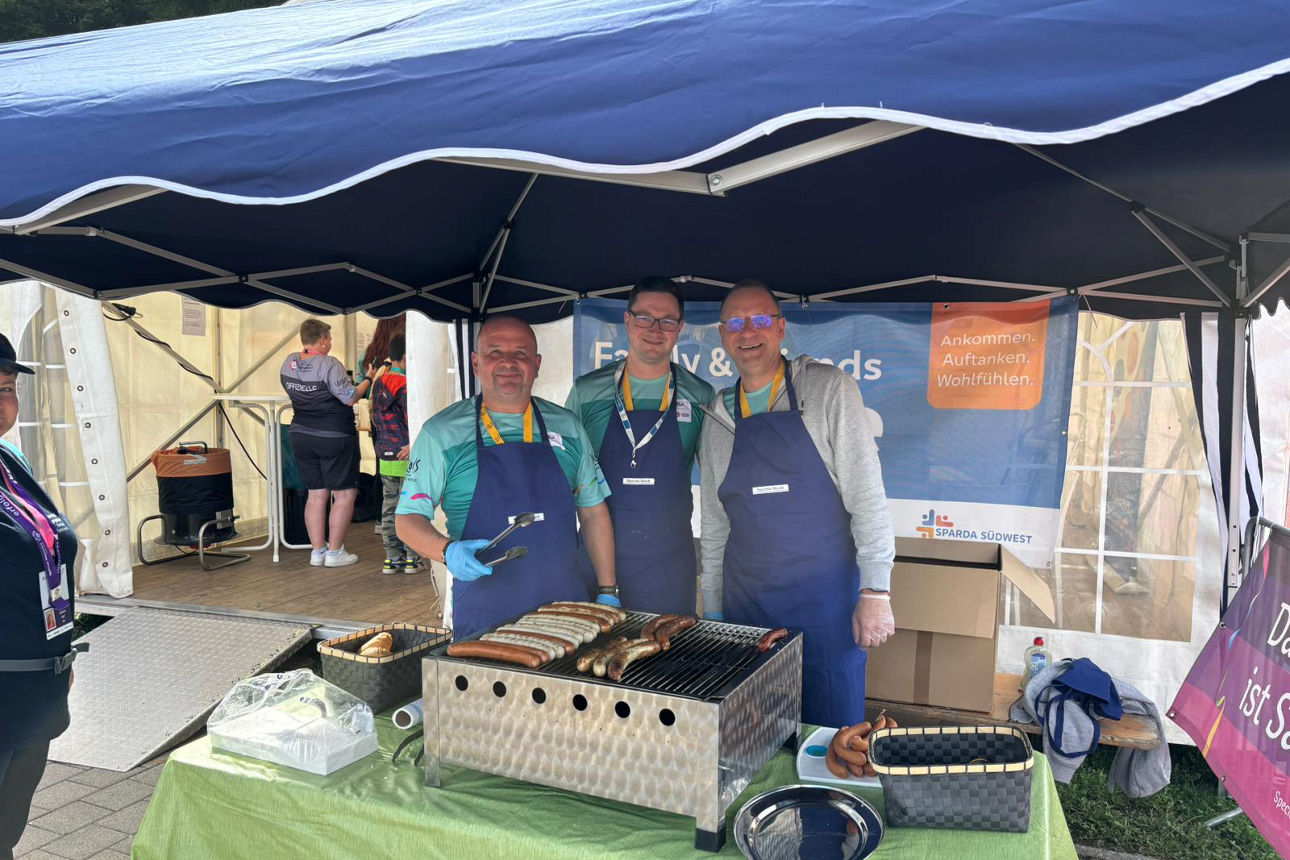 Drei Männer stehen in einem Pavillon hinter einem Grill