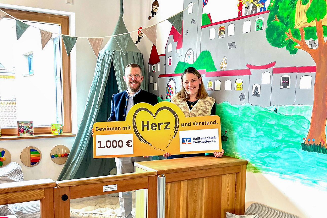Ein elegant gekleideter Mann überreicht einer Frau in einer Kinderbibliothek einen Scheck