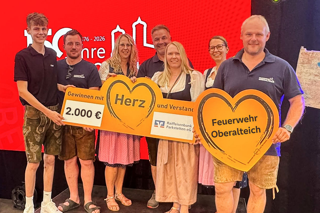 Zwei Männer überreichen einem anderen Mann einen symbolischen Scheck. 