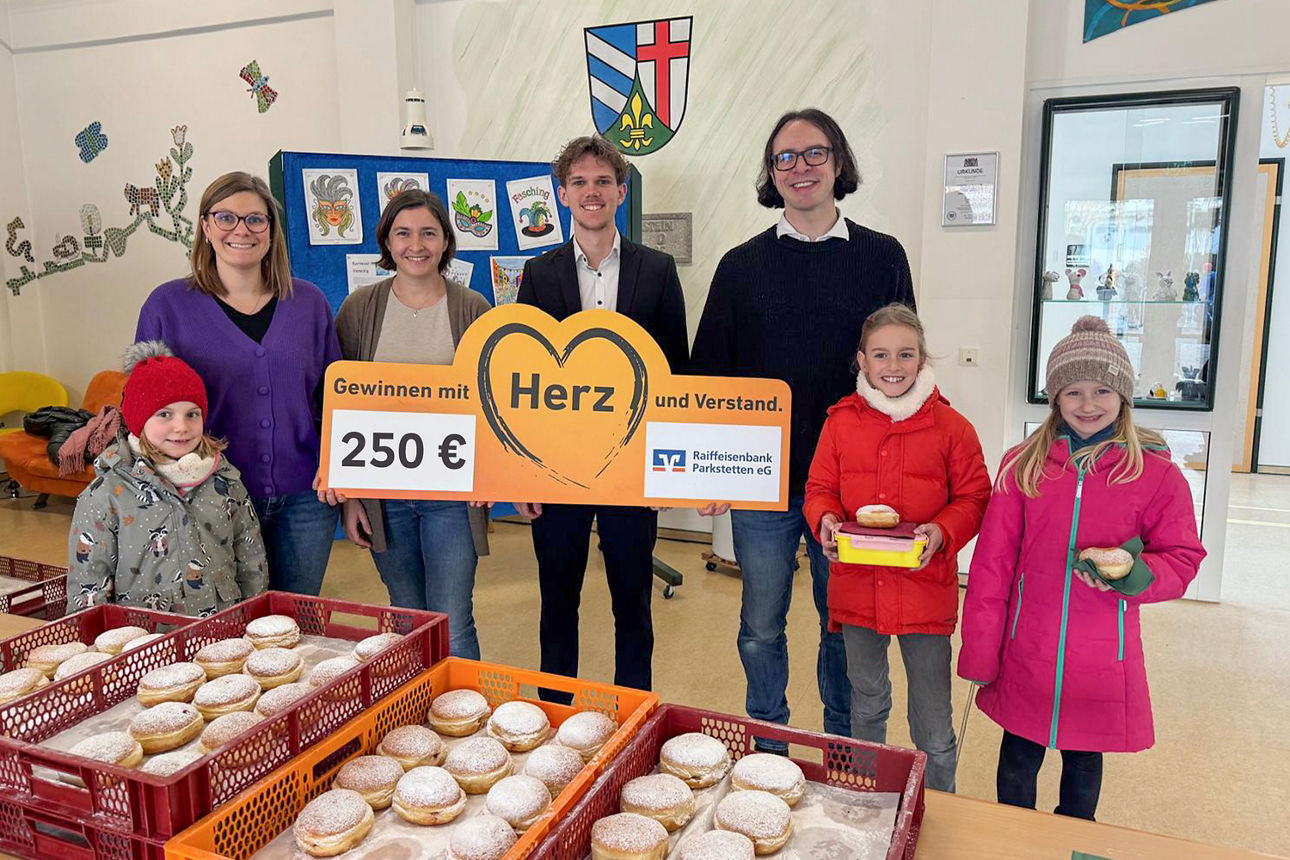 Gruppenfoto mit mehreren Erwachsenen und Kindern vor Kisten mit Krapfen