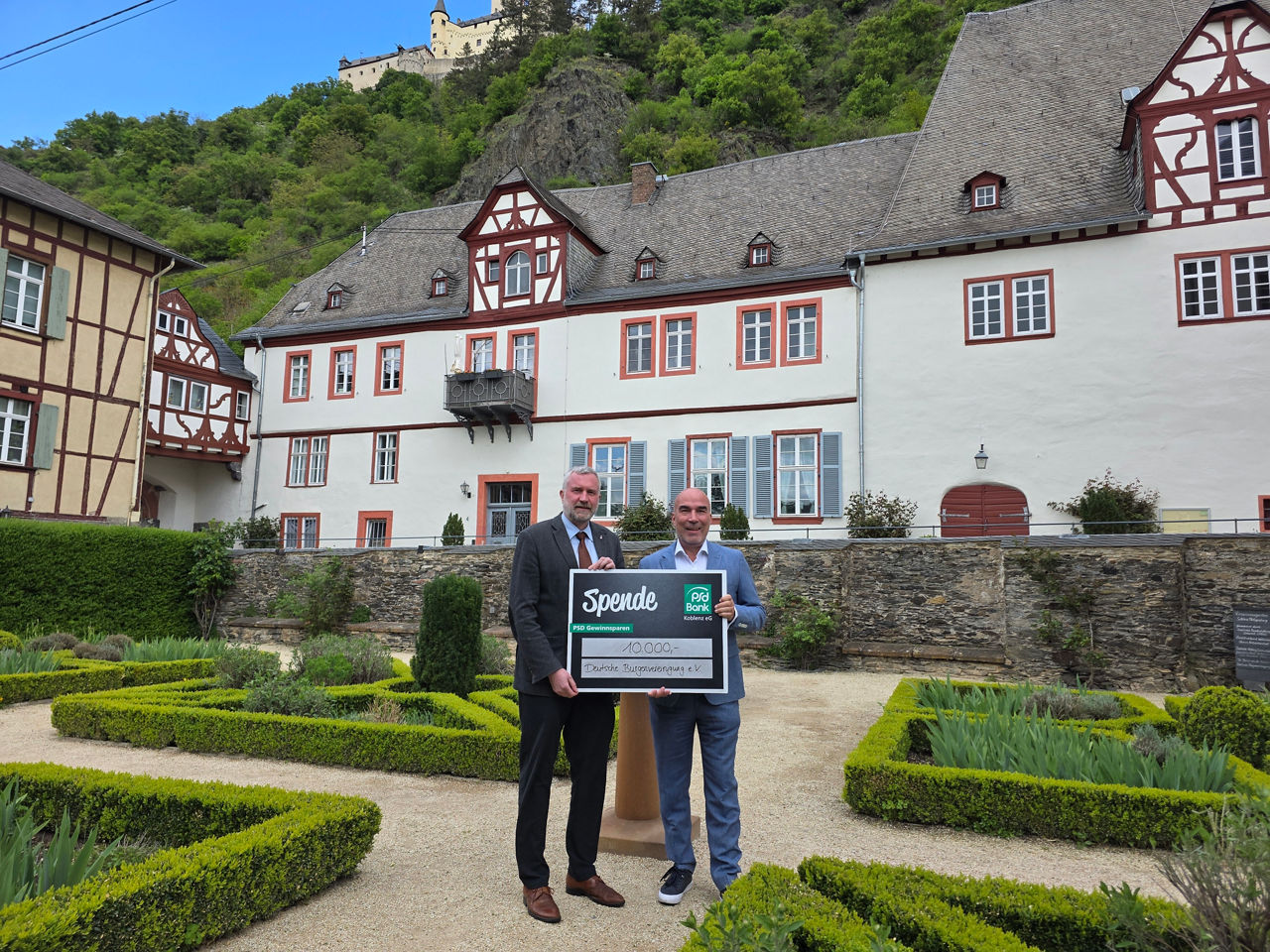 Mehrere Personen halten einen Scheck im Innenhof einer Burg