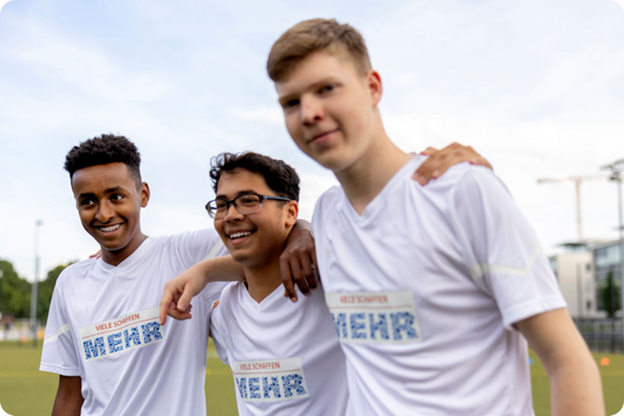 Drei Fußballjungs laufen lachend über den Platz und umarmen sich