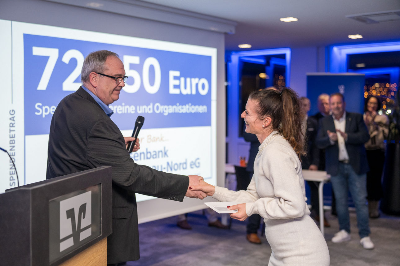 Ein Mann mit einem Mikrofon wärend er einer Frau die Hand reicht.