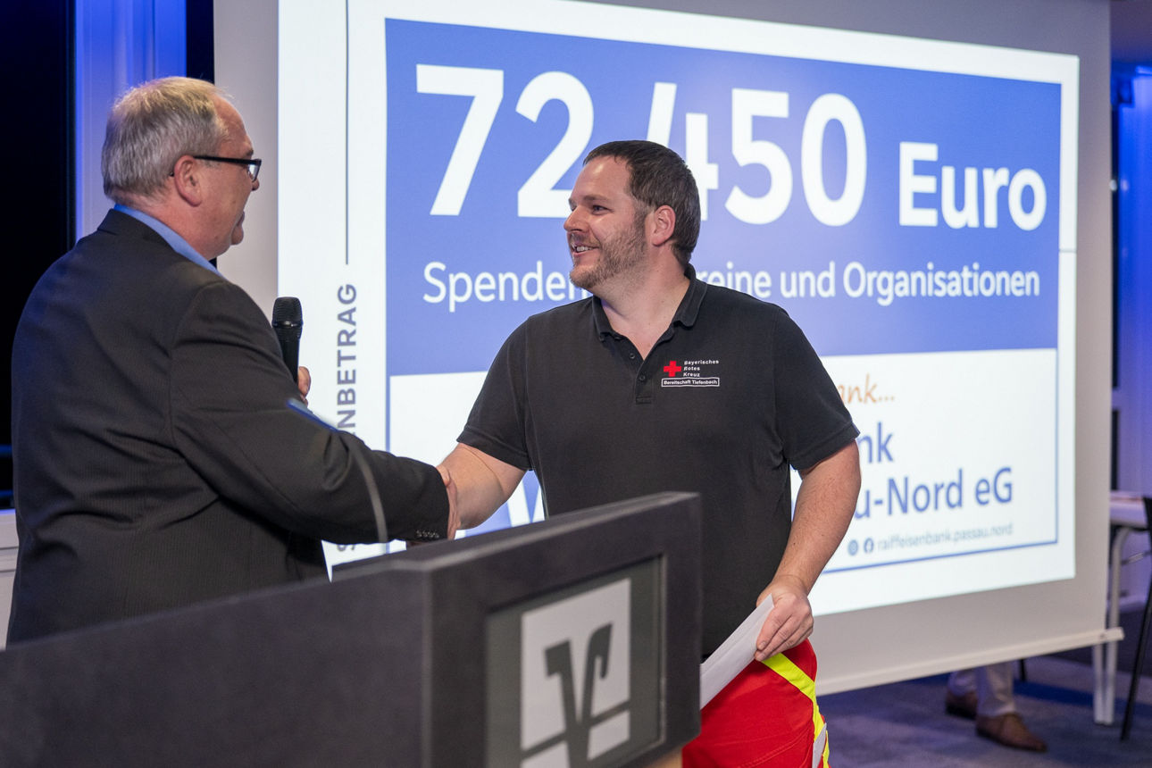 Ein Mann mit einem Mikrofon wärend er einem Mann die Hand reicht.