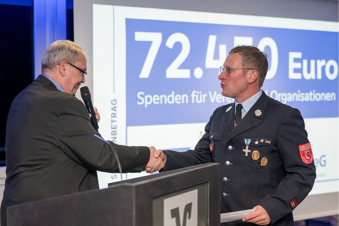 Ein Mann mit einem Mikrofon wärend er einem Mann die Hand reicht.