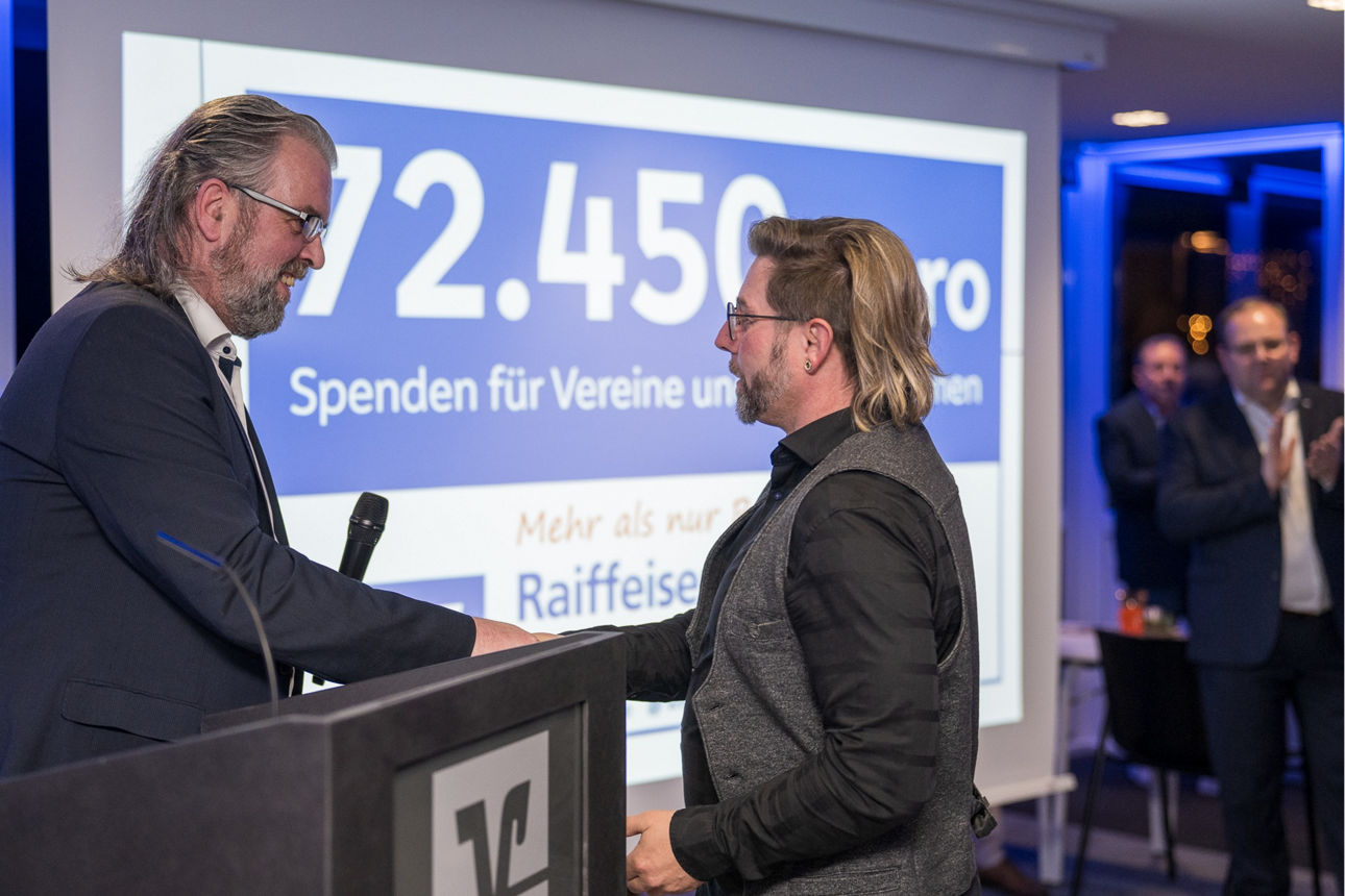 Ein Mann mit einem Mikrofon wärend er einem Mann die Hand reicht.